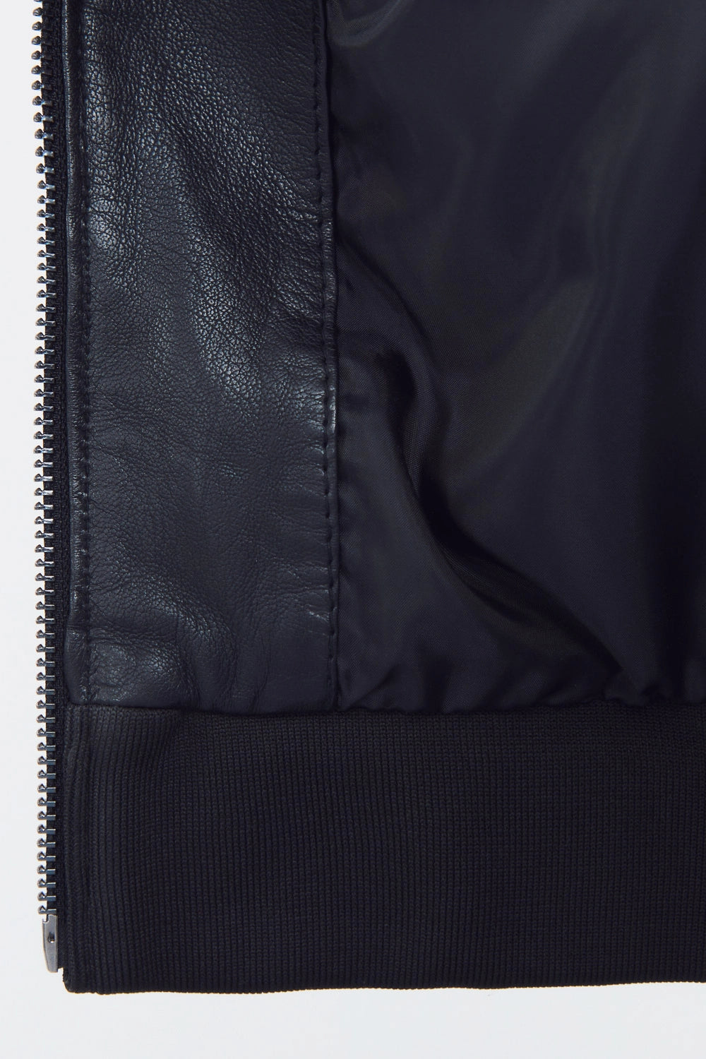 Front studio shot of a man wearing a slim-fit black leather bomber jacket with a snap-tab collar and zippered pockets, styled with dark pants against a white background.