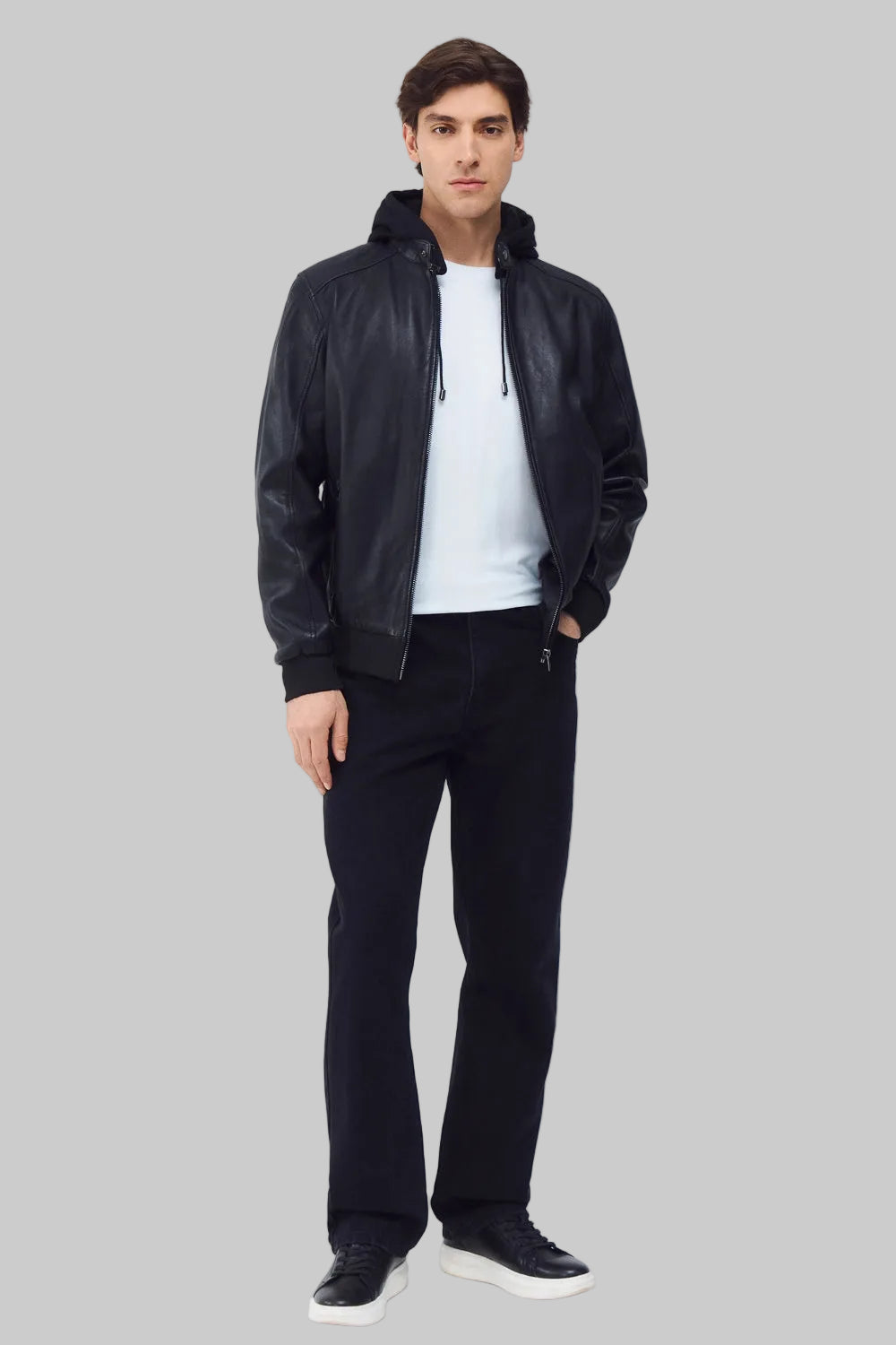 Front studio shot of a man wearing a slim-fit black leather bomber jacket with a snap-tab collar and zippered pockets, styled with dark pants against a white background.