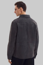 Front studio portrait of a man wearing a minimalist, charcoal gray suede shirt jacket snapped completely closed, featuring a clean concealed placket and point collar against a solid white background.