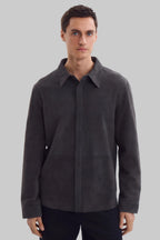 Front studio portrait of a man wearing a minimalist, charcoal gray suede shirt jacket snapped completely closed, featuring a clean concealed placket and point collar against a solid white background.