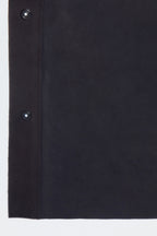 Front studio portrait of a man wearing a minimalist, charcoal gray suede shirt jacket snapped completely closed, featuring a clean concealed placket and point collar against a solid white background.